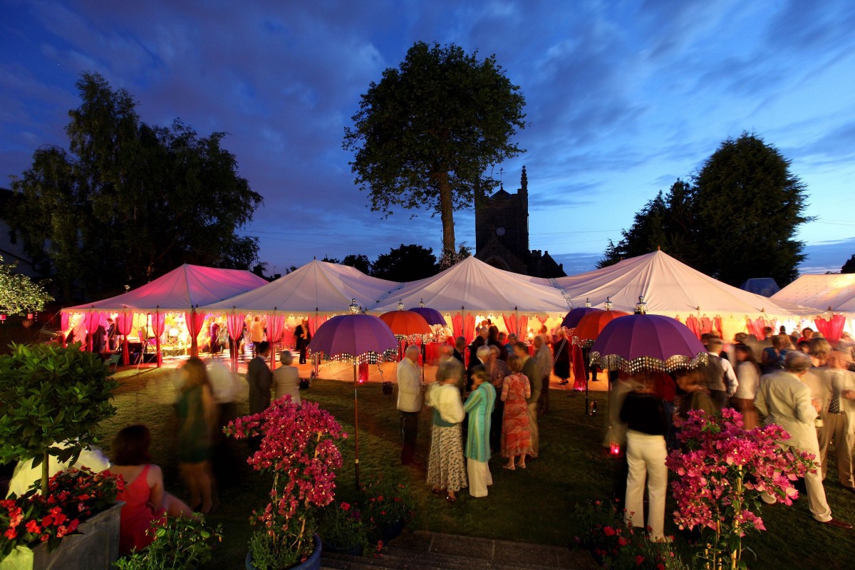 Guests mingle outside a Quadruple Maharaja wedding tent at dusk